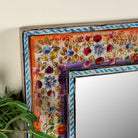 Close up image of a Taksha hand-painted reclaimed wood wall mirror with colourful floral artwork, blue border detailing, and vintage artisan character, 90x90cm.