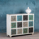 Side angle image of a carved mango wood chest of drawers with twelve multicolour floral drawer fronts, 124 × 40 × 102 cm.