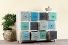 Side angle image with open drawers of a carved mango wood chest of drawers with twelve multicolour floral drawer fronts, 124 × 40 × 102 cm.