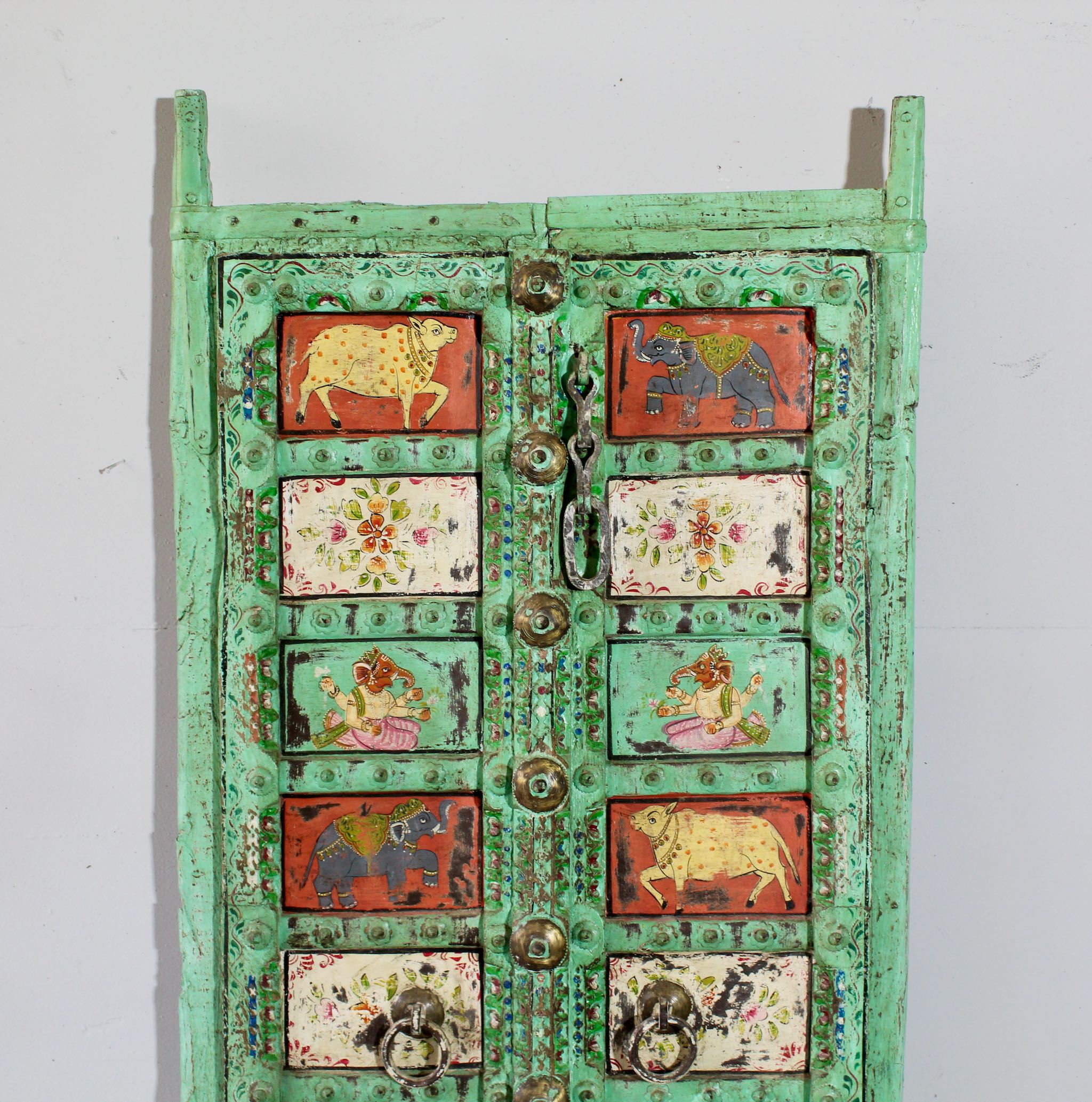 Close up image of a vintage Tarak hand-painted teak door panel with sacred and floral motifs in a distressed teal frame—a one-of-a-kind example of teak door panels and unique Indian wall decoration.