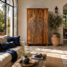 Lifestyle image of a Tash hand carved mango wood wardrobe with mandala carved doors, hanging rail and four storage compartments, 108x55x190cm