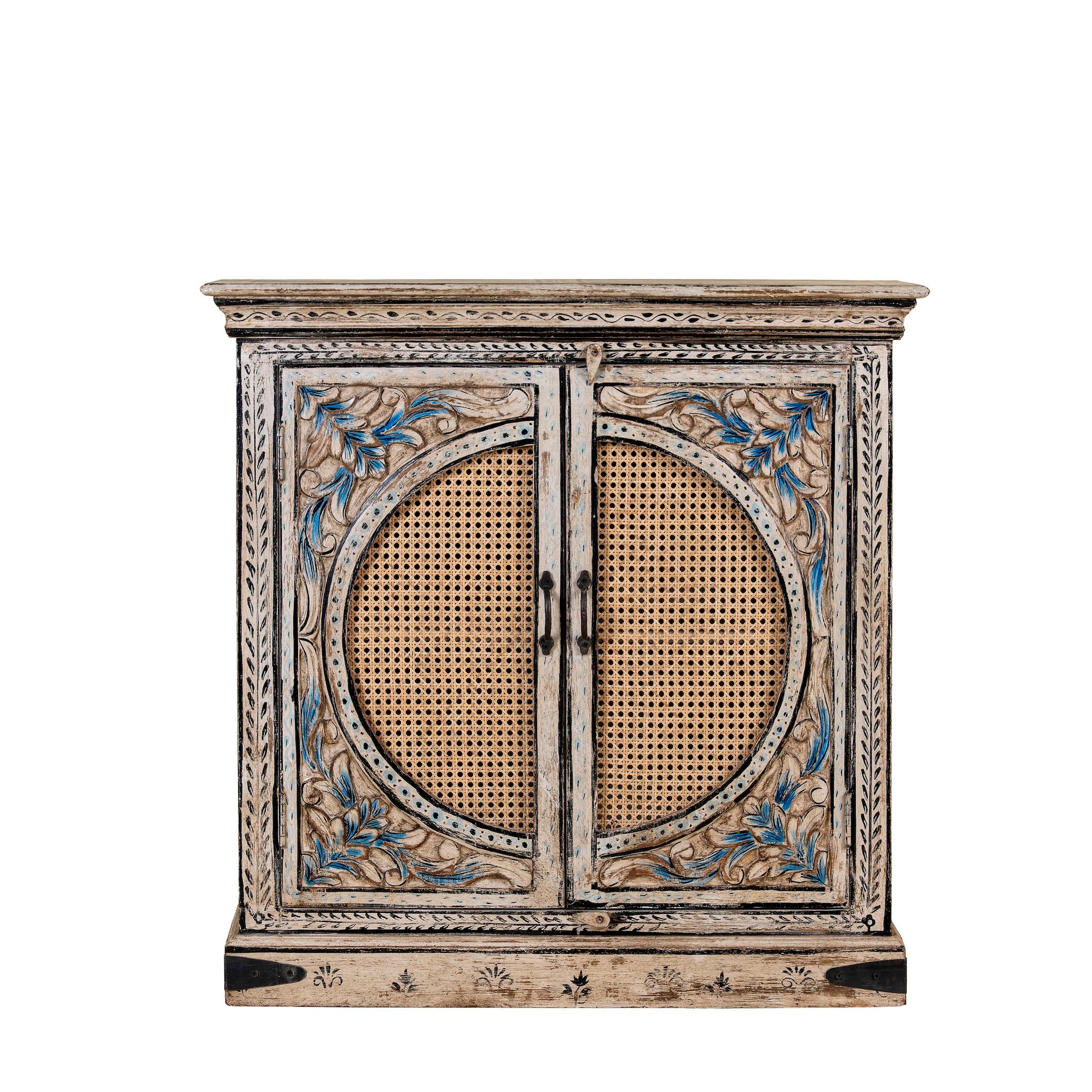 White Background view of a hand-made, hand-carved cupboard made of mango wood with blue floral designs, elephant motifs and rattan inserts.