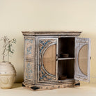 Open door view of a hand-made, hand-carved cupboard made of mango wood with blue floral designs, elephant motifs and rattan inserts.