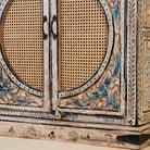 Close up view of a hand-made, hand-carved cupboard made of mango wood with blue floral designs, elephant motifs and rattan inserts.