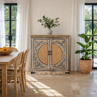 Lifestyle image of a hand-made, hand-carved cupboard made of mango wood with blue floral designs, elephant motifs and rattan inserts.