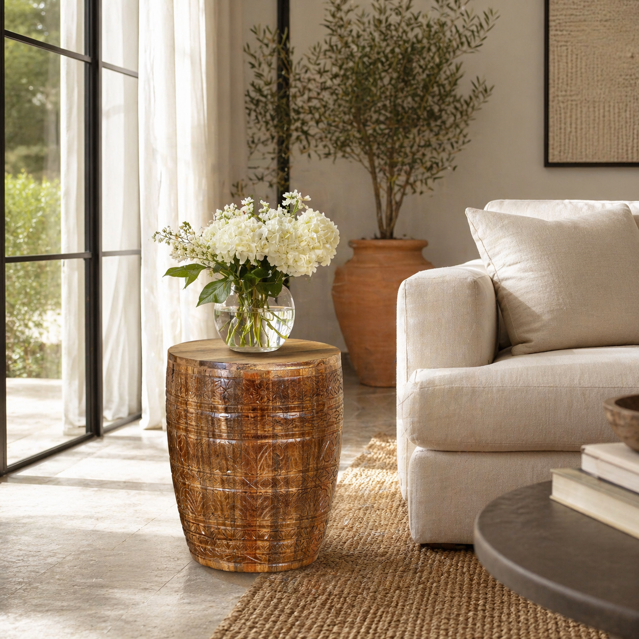 Life style image of a hand-carved mango wood coffee table with barrel shape and warm rustic finish; vintage style coffee table, 45 cm diameter, 55 cm height.