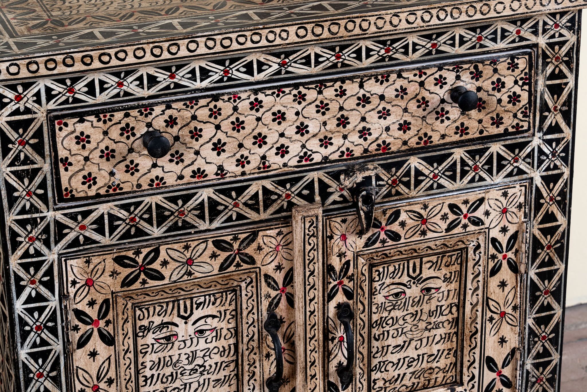 Close up image of a hand painted bedside cabinet made of reclaimed wood with one drawer and two doors in sanskrit style.