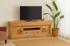Lifestyle imagination of a carved mango wood TV unit with hand-carved doors, one drawer, and open shelf, 150 × 60 × 40 cm.