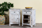 Side angle image with open doors of a pair of mango wood nightstands Uday with whitewashed vintage finish, featuring hand-carved geometric and floral designs. Each bedside table includes a drawer and cabinet for elegant and practical storage.