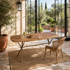 Lifestyle image of a Uddanda mango wood dining table featuring an intricately patterned natural wood tabletop with a brass-plated iron base and contemporary industrial design, 181cm.