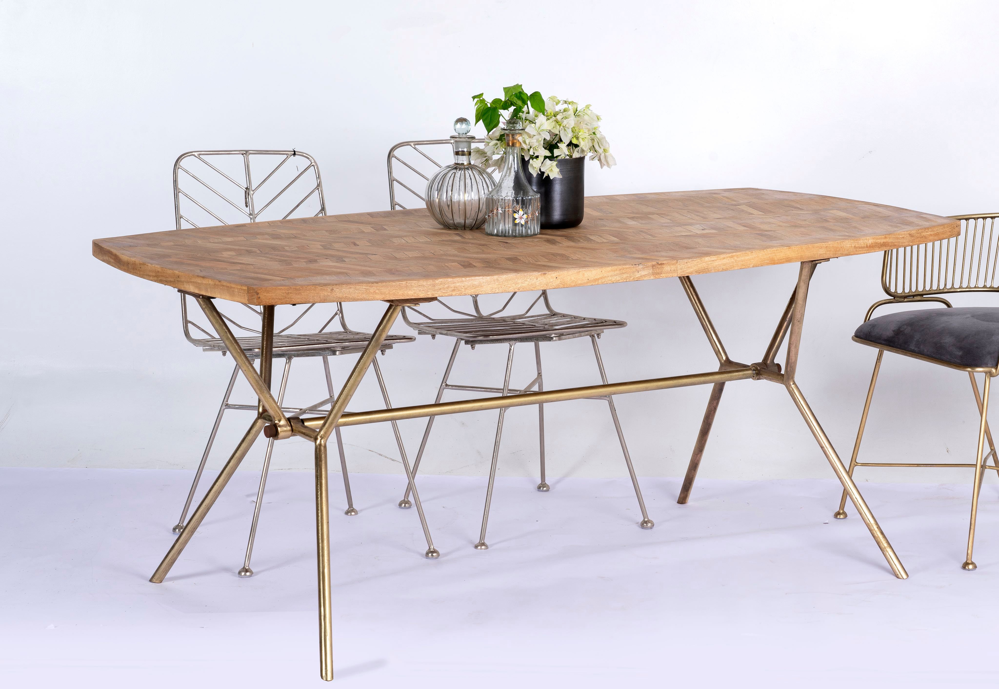 Side angle image of a Uddanda mango wood dining table featuring an intricately patterned natural wood tabletop with a brass-plated iron base and contemporary industrial design, 181cm.