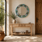 Lifestyle image of a Ujjwal hand-painted round reclaimed wood mirror with colourful floral artwork, turquoise vintage frame, and artisan detailing, 90cm diameter.