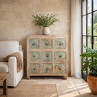 Lifestyle image of a hand-carved mango wood vintage chest of drawers with greenwashed floral fronts and antique white finish; perfect for bedroom furniture, 90 × 100 × 40 cm.