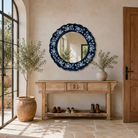 Lifestyle image of a Uttam hand-painted round reclaimed wood mirror with deep blue floral frame, vintage artisan detailing, 90cm diameter.