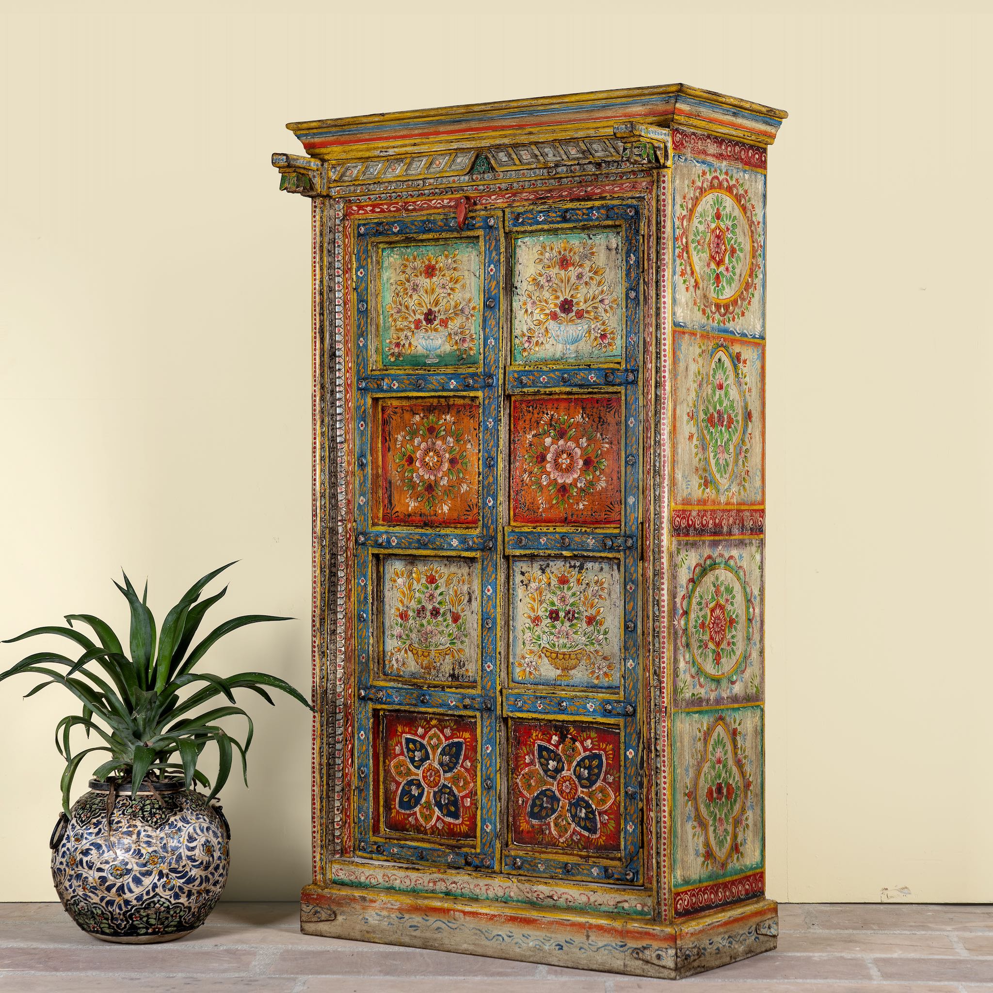 Side angle image of a and-painted teak wood cabinet with floral motifs; teak wood furniture for bohemian interiors, 105 × 55 × 177 cm.