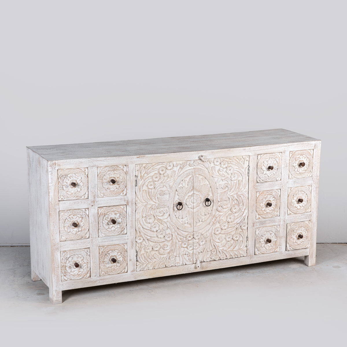 Side angle image of a Varnika white-washed mango wood sideboard with hand-carved front, six small drawers and two doors, 180x50x85cm