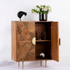 Side angle image with open doors of a natural mango wood cupboard with carved linear design and antique brass legs, 91 × 40 × 109 cm.