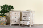 Side angle image with open drawers of a pair of mango wood nightstands Ved in a whitewashed vintage finish, featuring hand-carved drawer fronts with ornate circular and leafy motifs. Stylish and compact vintage-style bedside tables with three drawers for elegant storage.