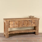 Side angle image of a Vihanraj reclaimed teak wood console table with original Indian door front, iron fittings and lower storage shelf 178cm