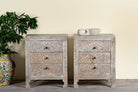 Lifestyle image of a pair of hand-carved mango wood nightstands Vikram with three drawers each, showcasing intricate floral motifs in a distressed vintage-style finish. Elegant and functional bedside tables with timeless artisan appeal.
