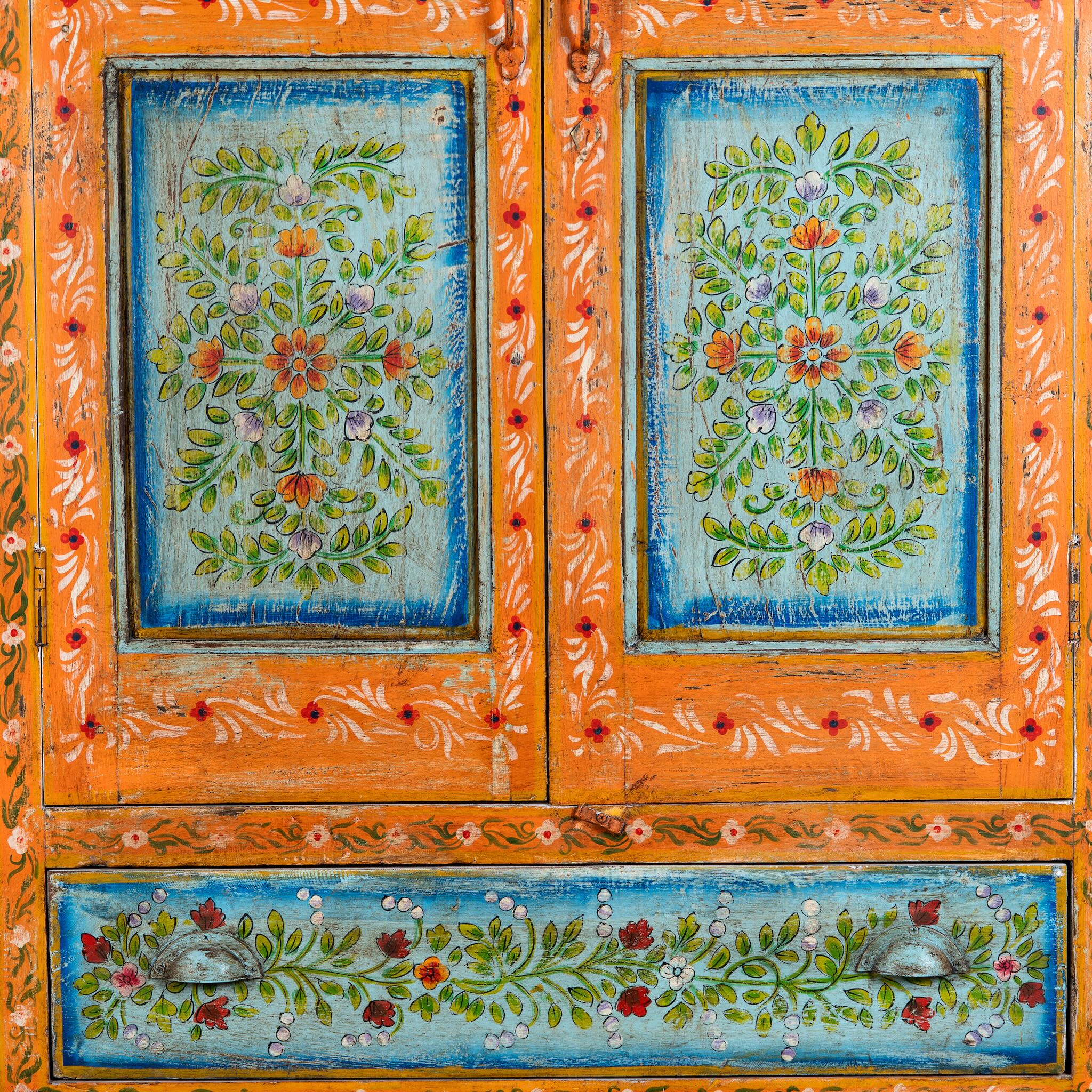 Close up image of a white background image of a hand-painted teak wood showcase with floral motifs and glass doors – sustainable furniture crafted from recycled wood with traditional Indian artistry.
