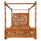 A traditional wooden canopy bed with intricate hand-carved floral and geometric patterns on the headboard and footboard, shown against a plain white background.