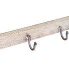 Close up image of a hand-carved reclaimed wood wall hook rack made from an antique Indian architectural element with five iron hooks, bleached finish, floral carvings, and vintage character, 150cm.