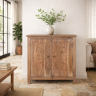 Lifestyle imagination of a carved acacia wood cupboard with floral cutout doors and brass knobs, 90 × 40 × 90 cm.