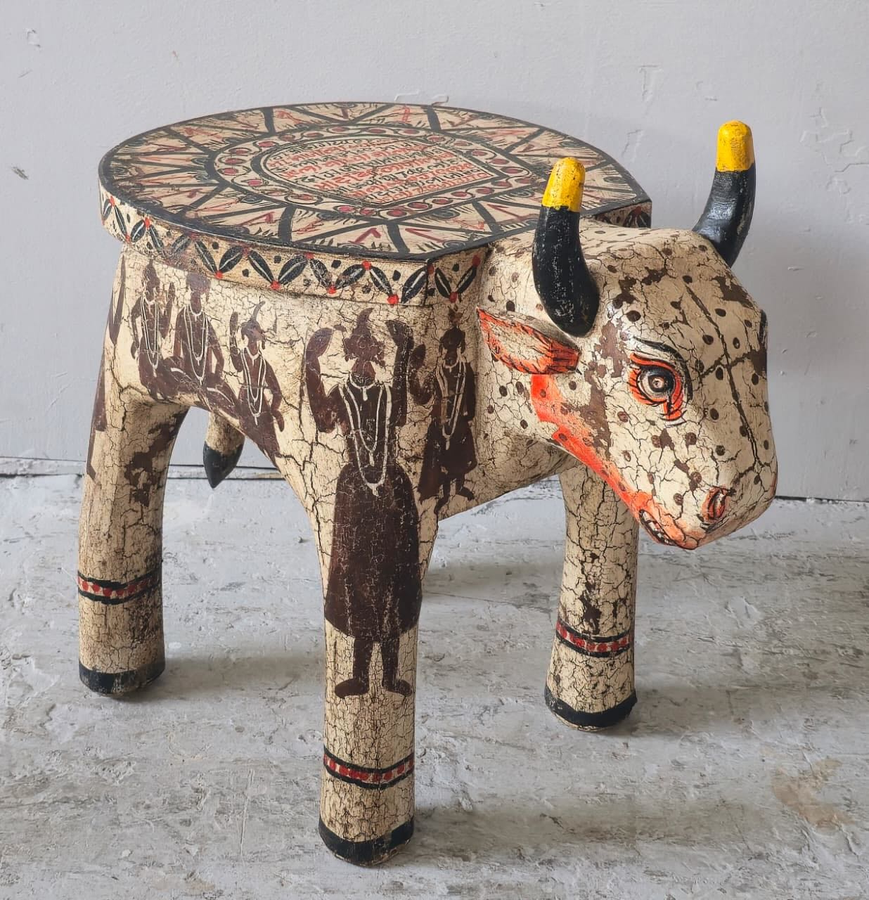 Hand-painted wooden cow-shaped side table with Indian script and blue folk art patterns, perfect for vintage and India-inspired home interiors.