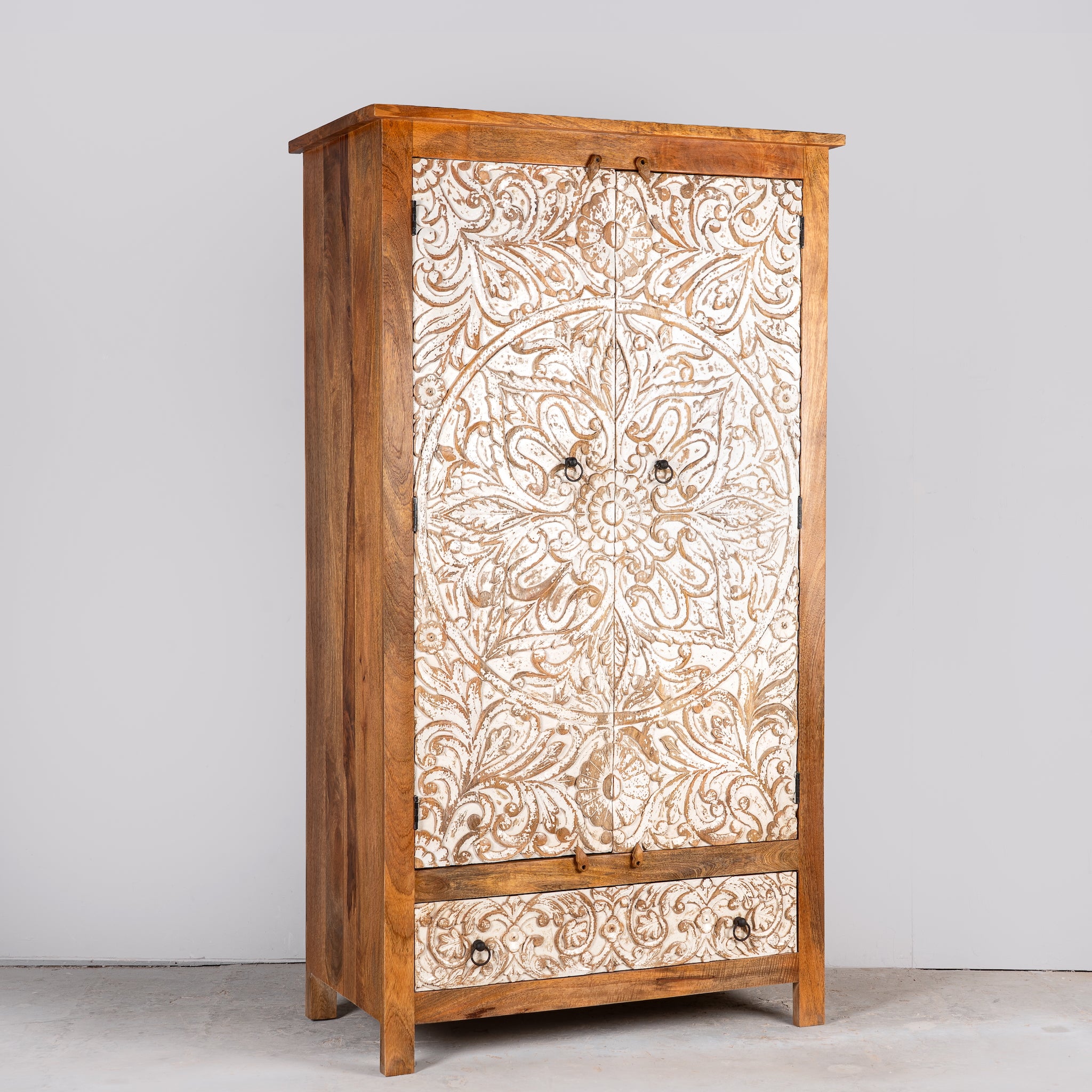 Side angle image of a hand-carved mango wood wardrobe with whitewashed floral motifs – Zashil by Om Home & Garden, a Mediterranean-inspired piece of carved wooden furniture.
