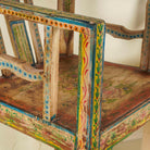 Arm rest of a hand-painted armchair crafted from reclaimed teak wood, featuring intricate traditional patterns in earthy tones on the backrest, seat, and frame, with a rustic and vintage finish.
