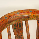 Close up image of the backrest of a hand-painted armchair crafted from reclaimed teak wood, featuring intricate traditional patterns in earthy tones on the backrest, seat, and frame, with a rustic and vintage finish.
