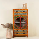 Hand-painted showcase cabinet made from mango wood, featuring a circular glass-front display, floral motifs in rich orange, green, and red tones, and five drawers for added storage.

