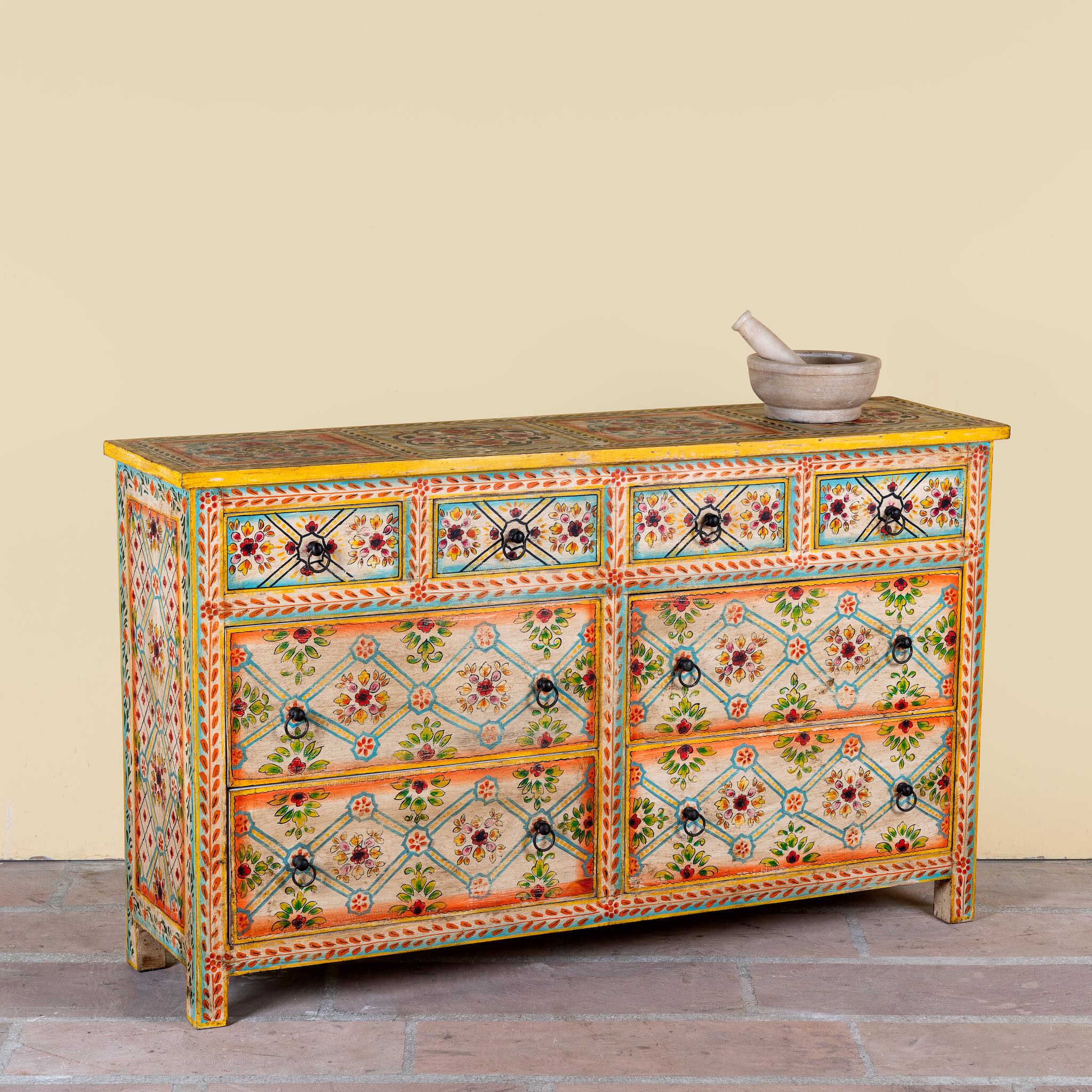 Side angle image of a Ziya hand‑painted chest of 8 drawers made from reclaimed wood with floral motifs and iron handles—an artisan piece of painted wooden furniture.