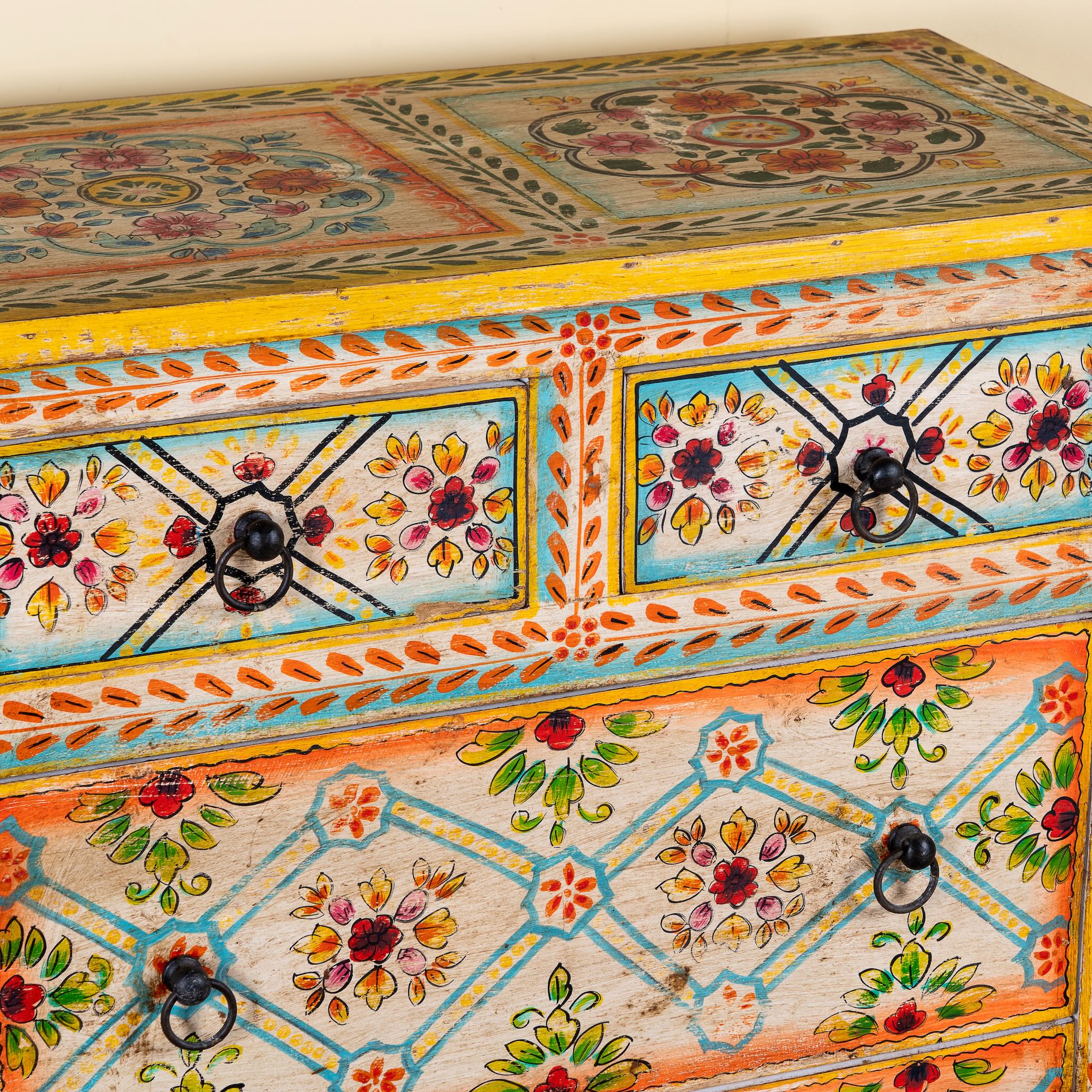 Close up image of a Ziya hand‑painted chest of 8 drawers made from reclaimed wood with floral motifs and iron handles—an artisan piece of painted wooden furniture.