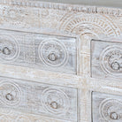 Close up image of a handcrafted chest of drawers Zuber made from reclaimed wood, featuring six carved drawers with circular motifs and a whitewashed finish. A rustic, sustainable furniture piece with soft texture and elegant detailing.