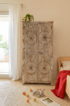 Lifestyle image of a hand-carved acacia wood wardrobe with floral detailing and distressed finish – vintage living room furniture with artisan craftsmanship.