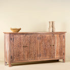 Side view of an acacia wood sideboard with floral carvings over all 4 doors and brass fitted door handles.