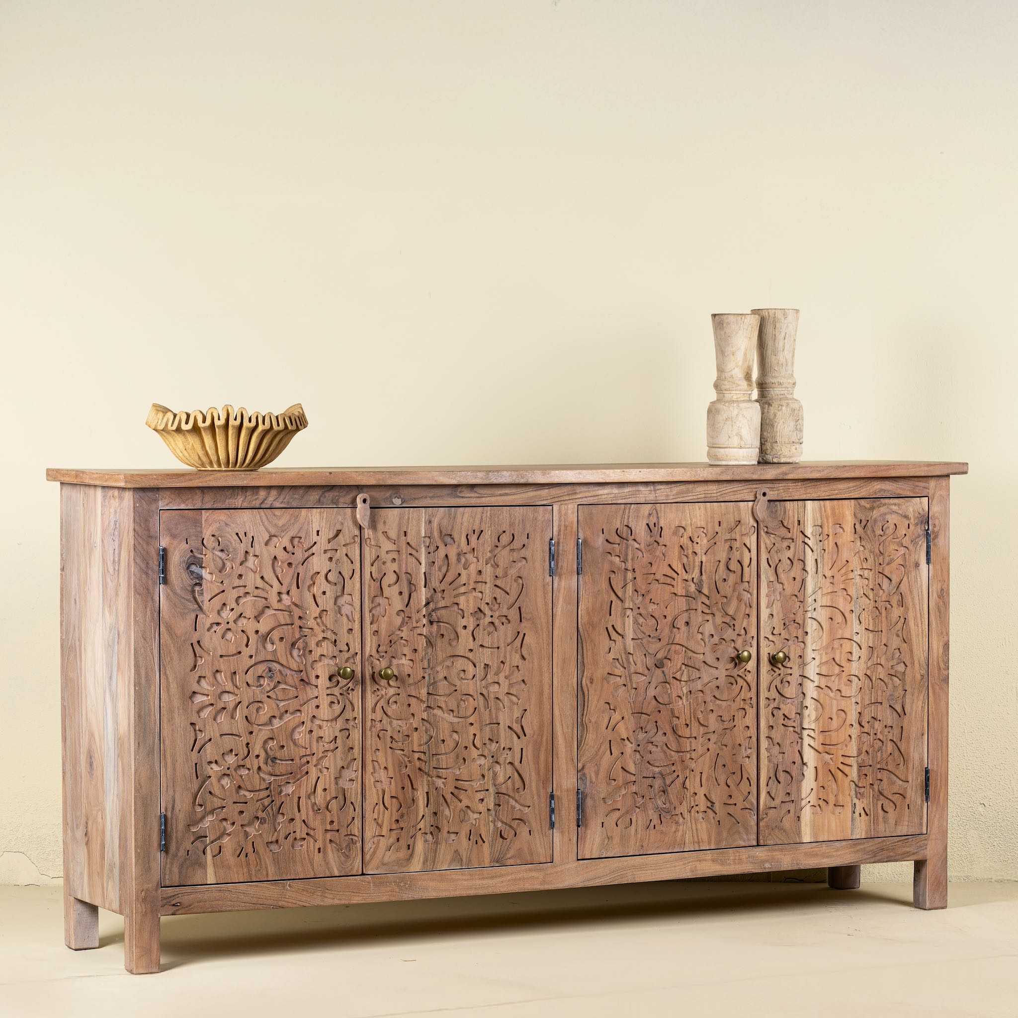 Side view of an acacia wood sideboard with floral carvings over all 4 doors and brass fitted door handles.