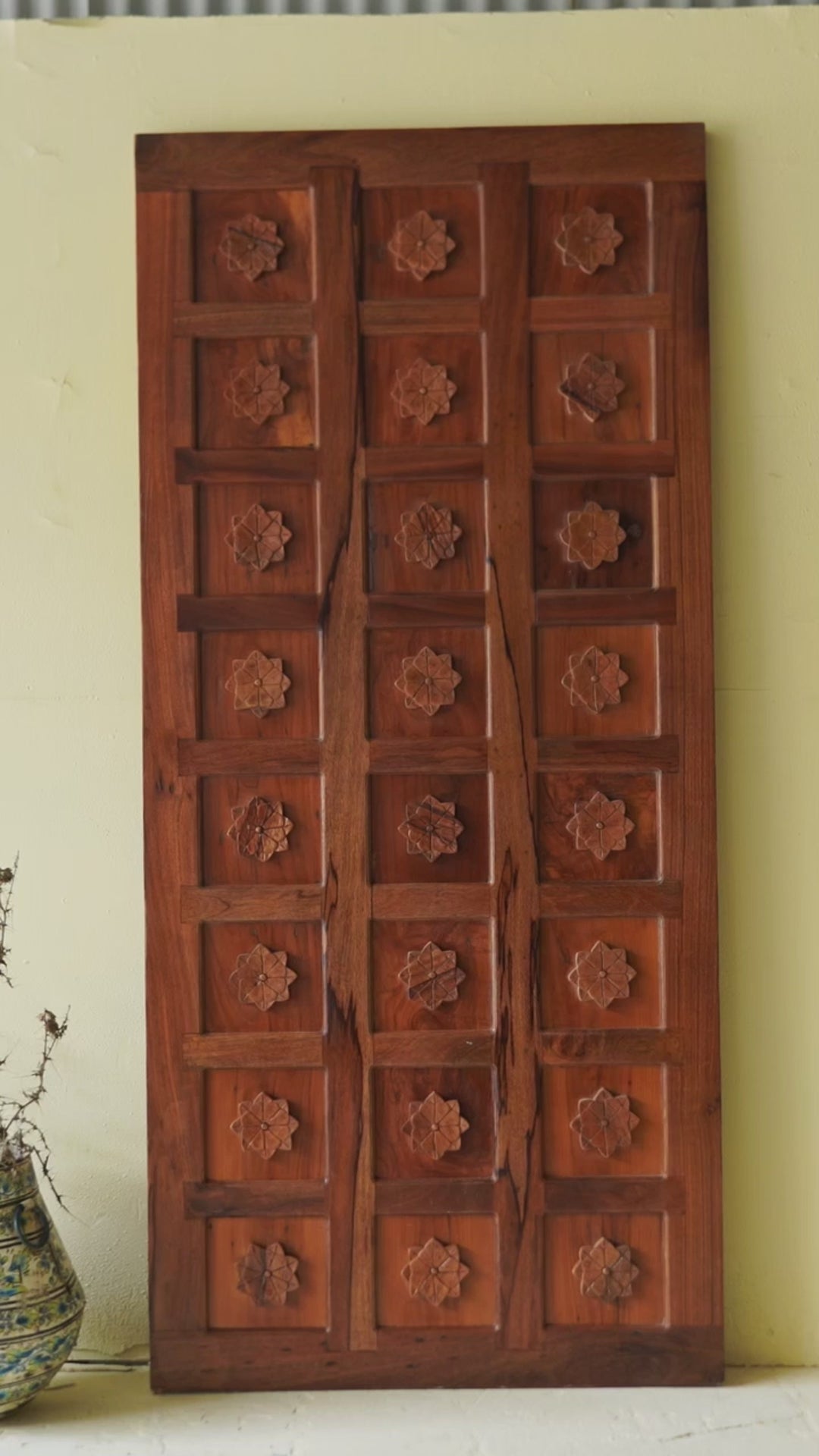 Hand-carved sliding door panel made from reclaimed wood, featuring symmetrical floral motifs in square reliefs for a warm, artisanal statement piece.
