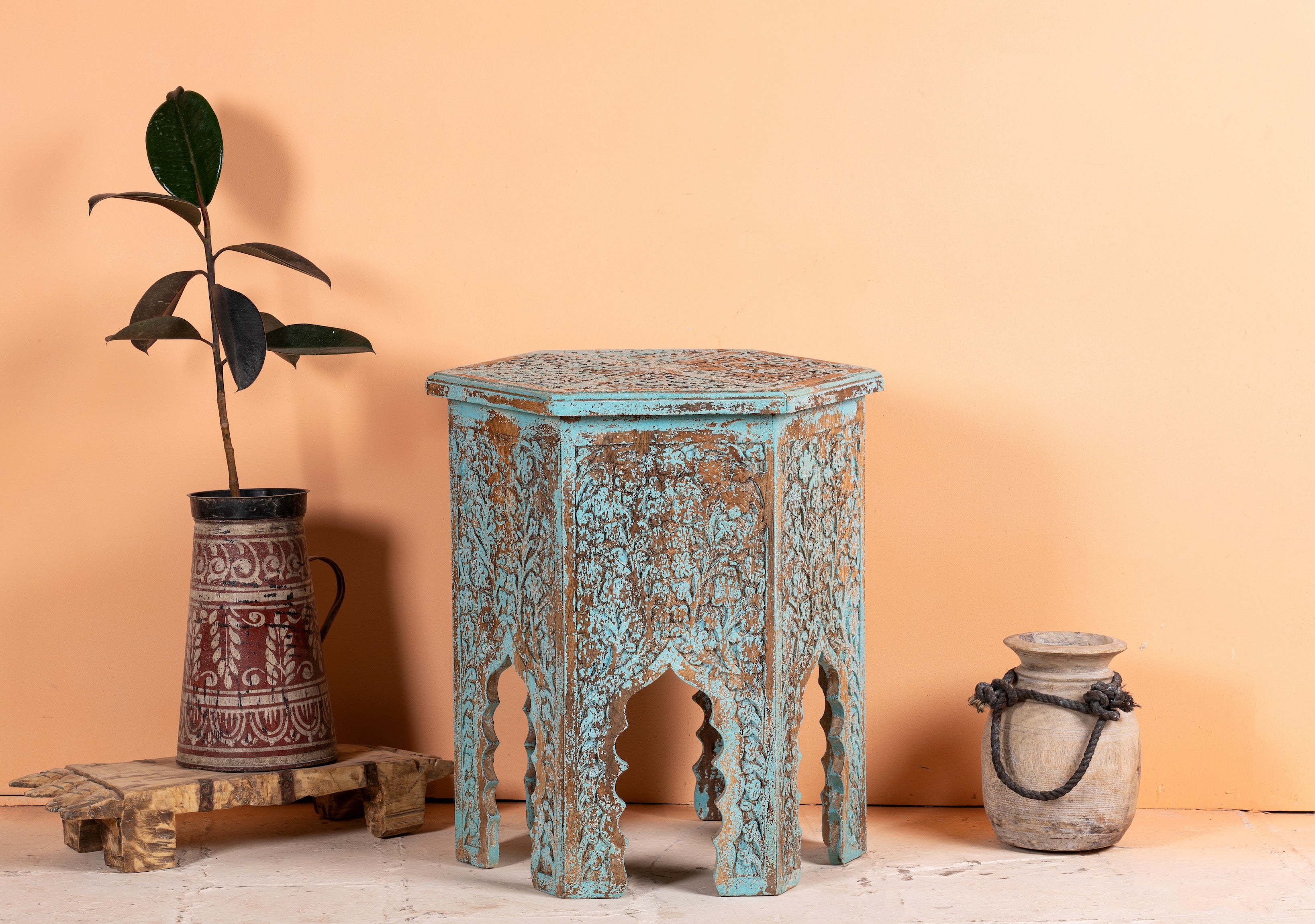 A hand-carved mango wood coffee table with a blue washed effect and traditional Moroccan design, displayed with decorative vases and a plant.