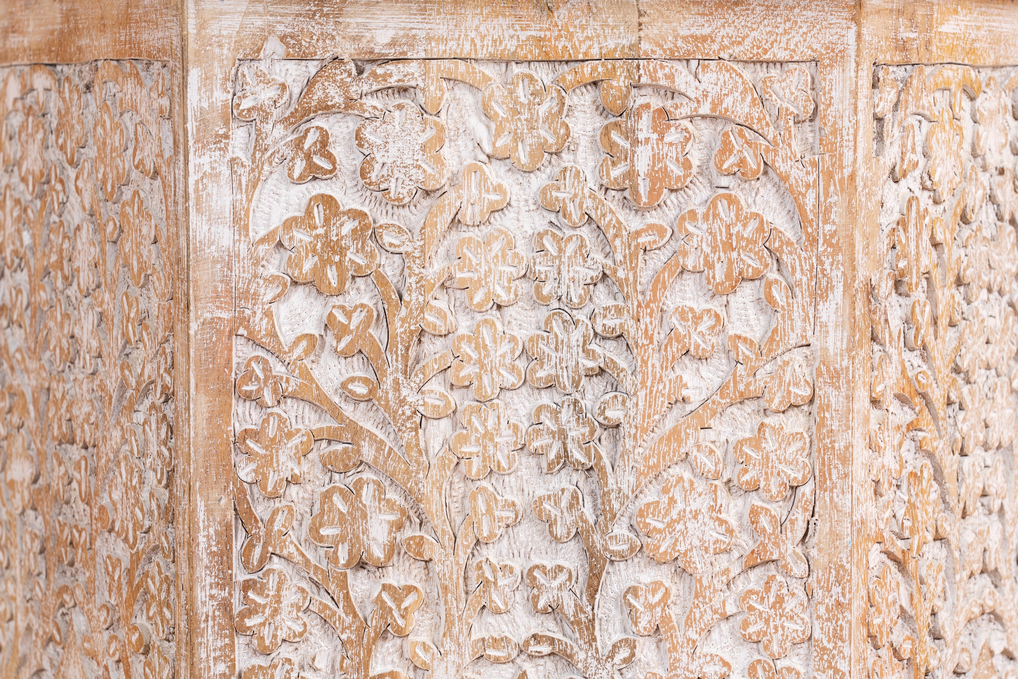 Close up image of a hand carved white washed vintage coffee table with floral motif.