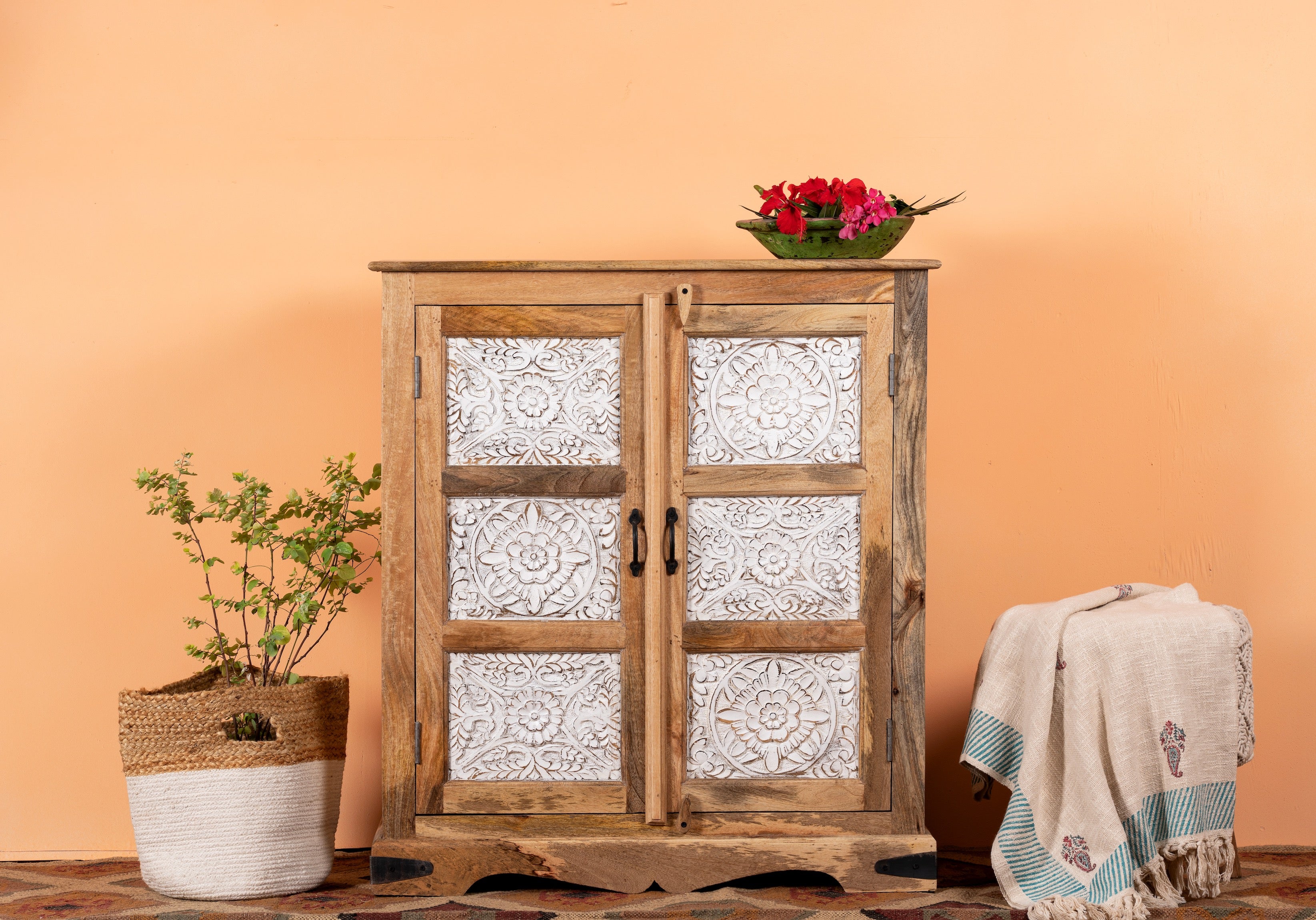 A handcrafted Indian cupboard made of natural mango wood with white floral engravings on the front, two doors, and a decorative item on top.