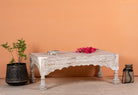 Side angle image of a Dhola handcrafted solid mango wood coffee table with intricately hand-carved floral patterns, natural wood grain, and artisan craftsmanship, 120cm.