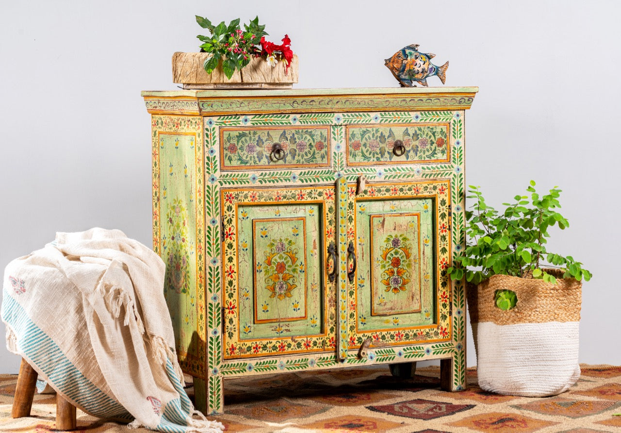 Side angle image of a hand painted green Indian cabinet made from recycled wood with floral motifs, 2 drawers and 2 compartments, 90 × 90 × 40 cm.