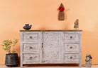 Life style image of a handcrafted mango wood sideboard with carved floral motifs, whitewashed base and natural top; perfect for vintage home decor and living room furniture, 150 × 40 × 90 cm.